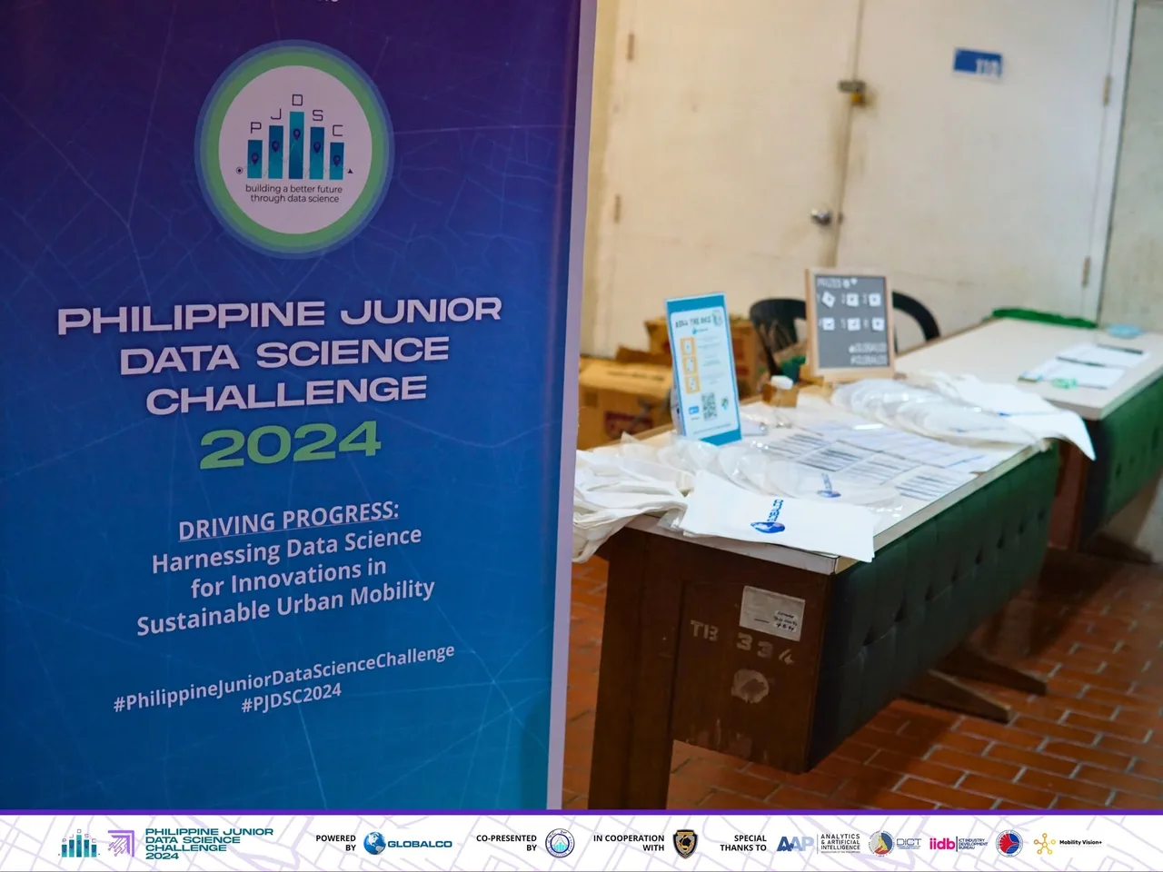 The PJDSC 2024 standee beside the registration table at the DICT office, with GlobalCo tote bags and prize cards laid out.