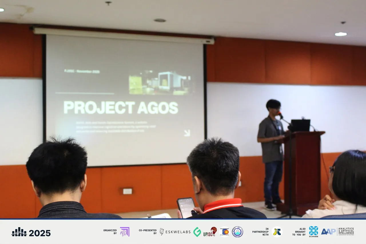 A finalist presenting Project AGOS from the lectern, with the project title on the screen.