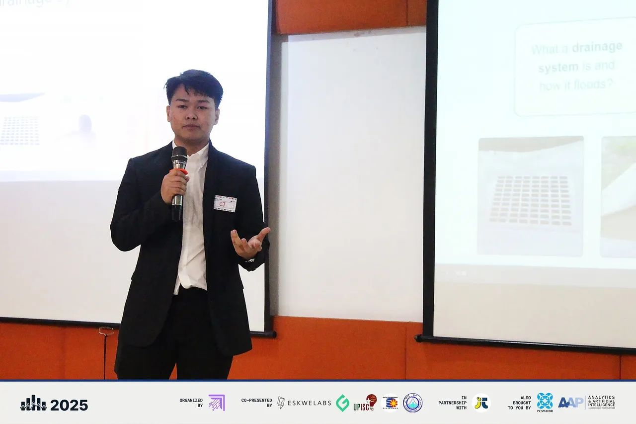 A finalist in a suit presenting with a microphone in front of the projector screen.